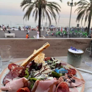 Assiette de charcuterie avec vue sur la mer et les palmiers à Nice pendant un apéro Oncity no-video