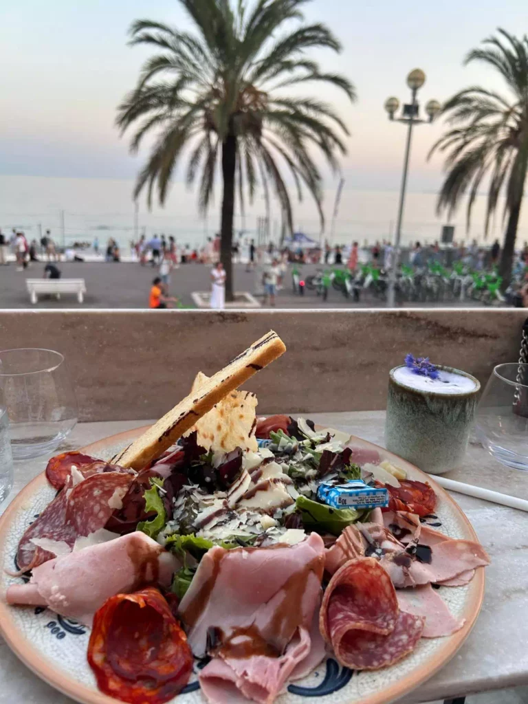 Assiette de charcuterie avec vue sur la mer et les palmiers à Nice pendant un apéro Oncity no-video